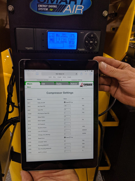 Photo of a person holding a tablet with the EMAX E550 Series 10 HP Air Compressor's settings on the screen, with the compressor in the background.