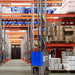 A blue and grey industrial Airrex Dehumidifier ADH-8000 on wheels, positioned in a warehouse aisle with tall storage racks holding various products.